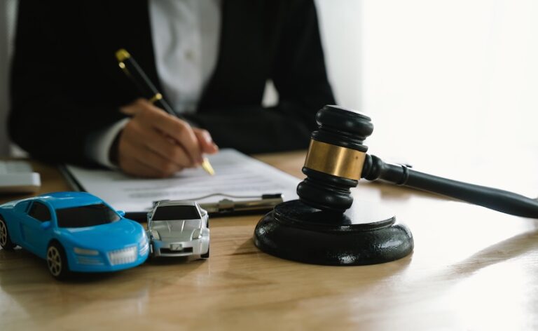 An attorney from Panchenko Law Firm in a dark suit signs documents on a desk beside two toy cars positioned in a collision and a judge's gavel- illustrating the legal documentation stage of the car accident claim process when an attorney is involved in pursuing compensation.