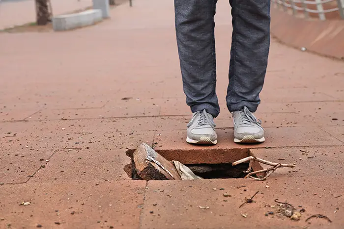 person standing near a hole in the sidewalk
