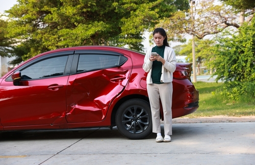 Woman standing beside her wrecked red car after a multi-car accident in Matthews, NC, symbolizing the need for legal help from a car accident lawyer.