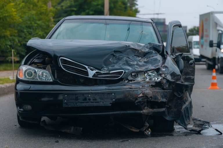 A severely damaged black sedan with a crushed front end and deployed airbag requiring a car accident lawyer consultation from Panchenko Law Firm.