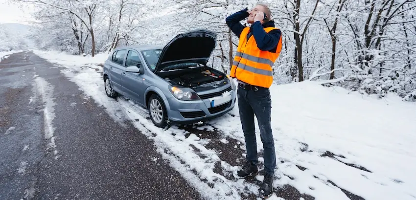 Common car wrecks, such as this one, happen often in the snow. This male is on the side of the road calling for help with his car behind him.