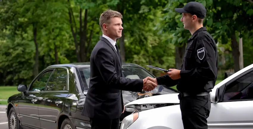 A professional businessman is shaking hands with a police officer and is documenting a local car accident attorney case at the crash scene in Charlotte NC.