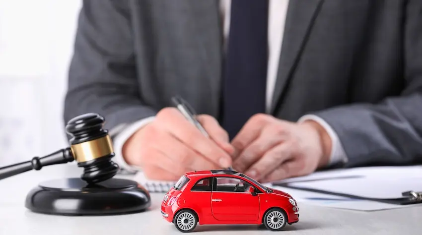A lawyer is reviewing car accident claim documents with a gavel and red toy vehicle on a desk at Panchenko Law Firm in Charlotte NC.