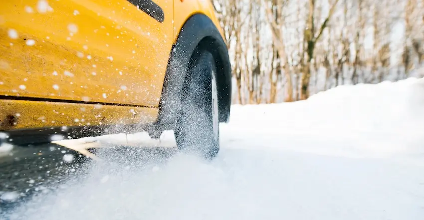 A yellow car is driving through snowy conditions where weather-related car accident claims are common in Charlotte NC.