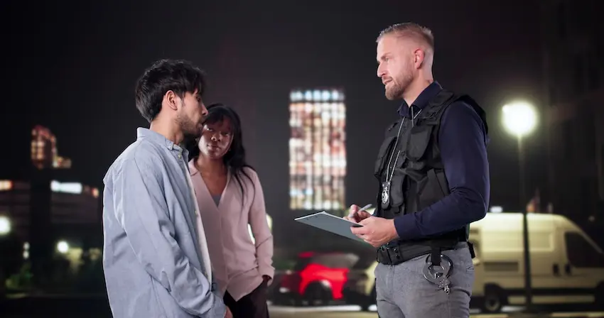 A police officer in a tactical vest takes notes on a clipboard while speaking with two individuals at night in an urban parking lot in front of a white van depicting the official documentation process that serves as the foundation for car accident claims for Panchenko Law Firm in Charlotte NC.
