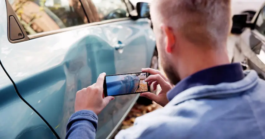 A man is photographing vehicle damage with his smartphone to document evidence after a car accident for insurance claim in Spartanburg.