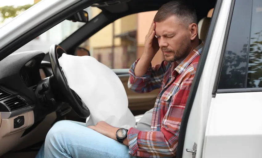 A injured driver is holding his head in pain with a deployed airbag visible after experiencing a car accident collision in Charlotte.