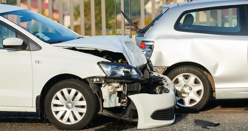 A white car with its entire front end crushed and bumper torn away sits pressed against the rear of another white vehicle on a city street with debris on the pavement depicting the type of serious rear-end collision that entitles injured victims to pursue compensation benefits- with help from Panchenko Law Firm- for property damage- medical expenses- and lost wages in Charlotte NC.