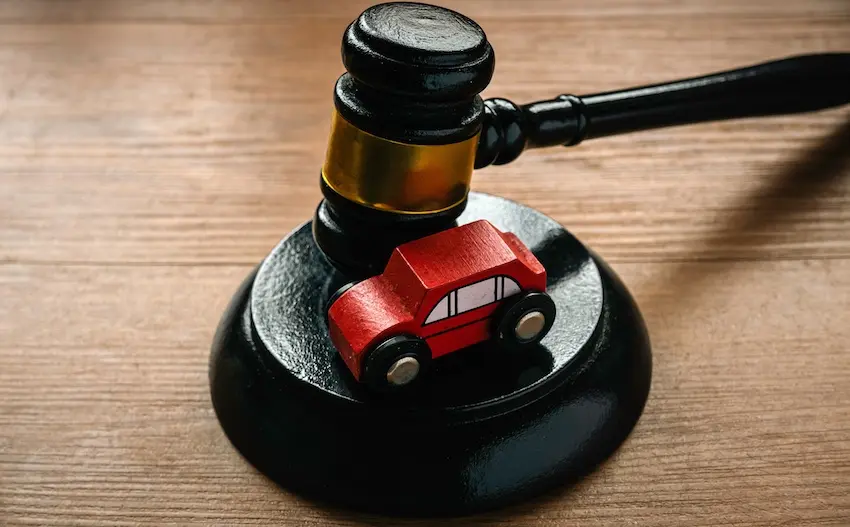 A small red wooden toy car sits centered on a round black judge's gavel sound block with the dark gavel head resting directly on top of it against a wood grain background representing the legal authority that courts exercise in awarding compensation benefits to accident victims who cannot reach a fair settlement with an insurance carrier in Spartanburg SC.