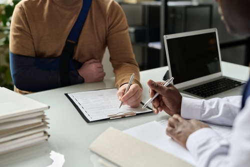 A man in an arm sling is signing legal documents with a rideshare accident lawyer after a rideshare accident.